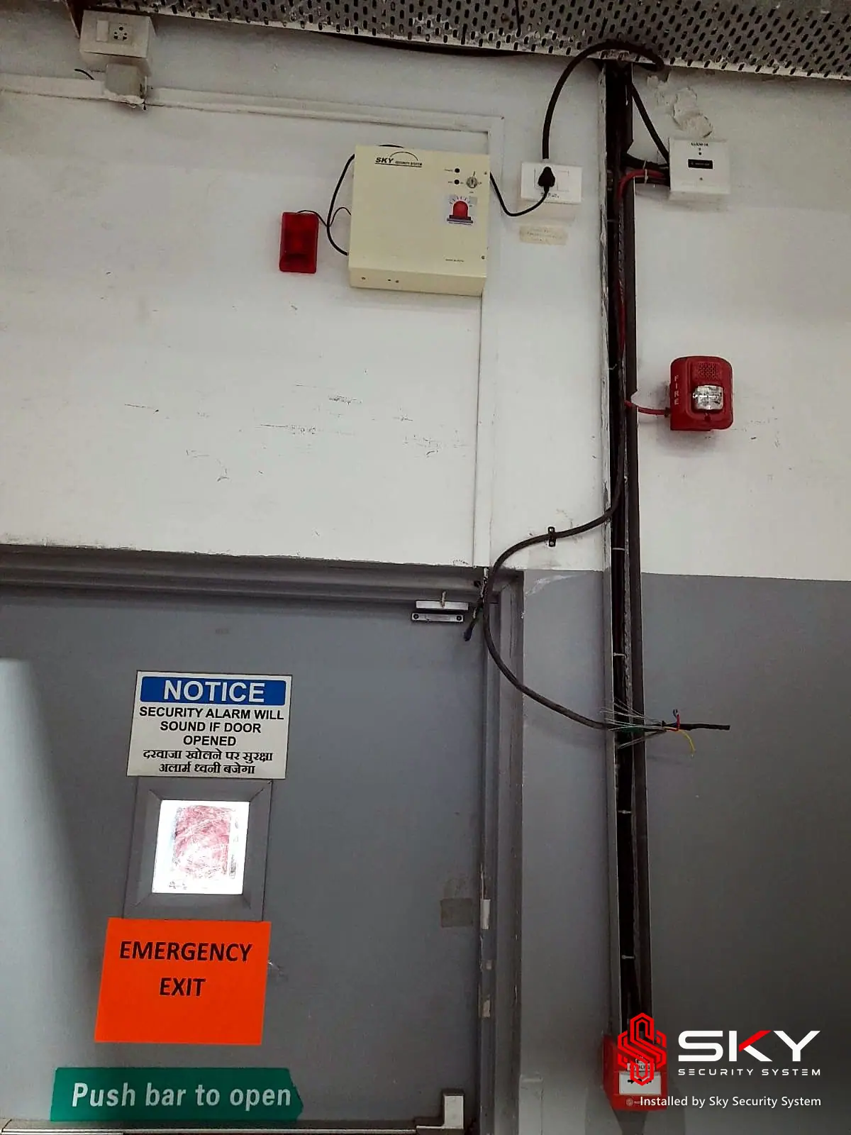 Fire alarm devices beside an emergency exit door at an industrial plant, Chakan, Pune. Security and ELV work by Sky Security System.